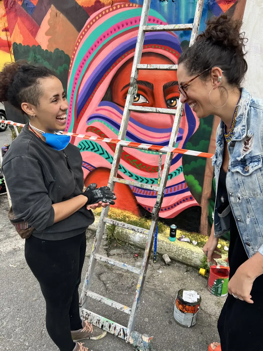 Duas mulheres conversam diante de mural colorido da Favela Galeria, na Vila Flávia.