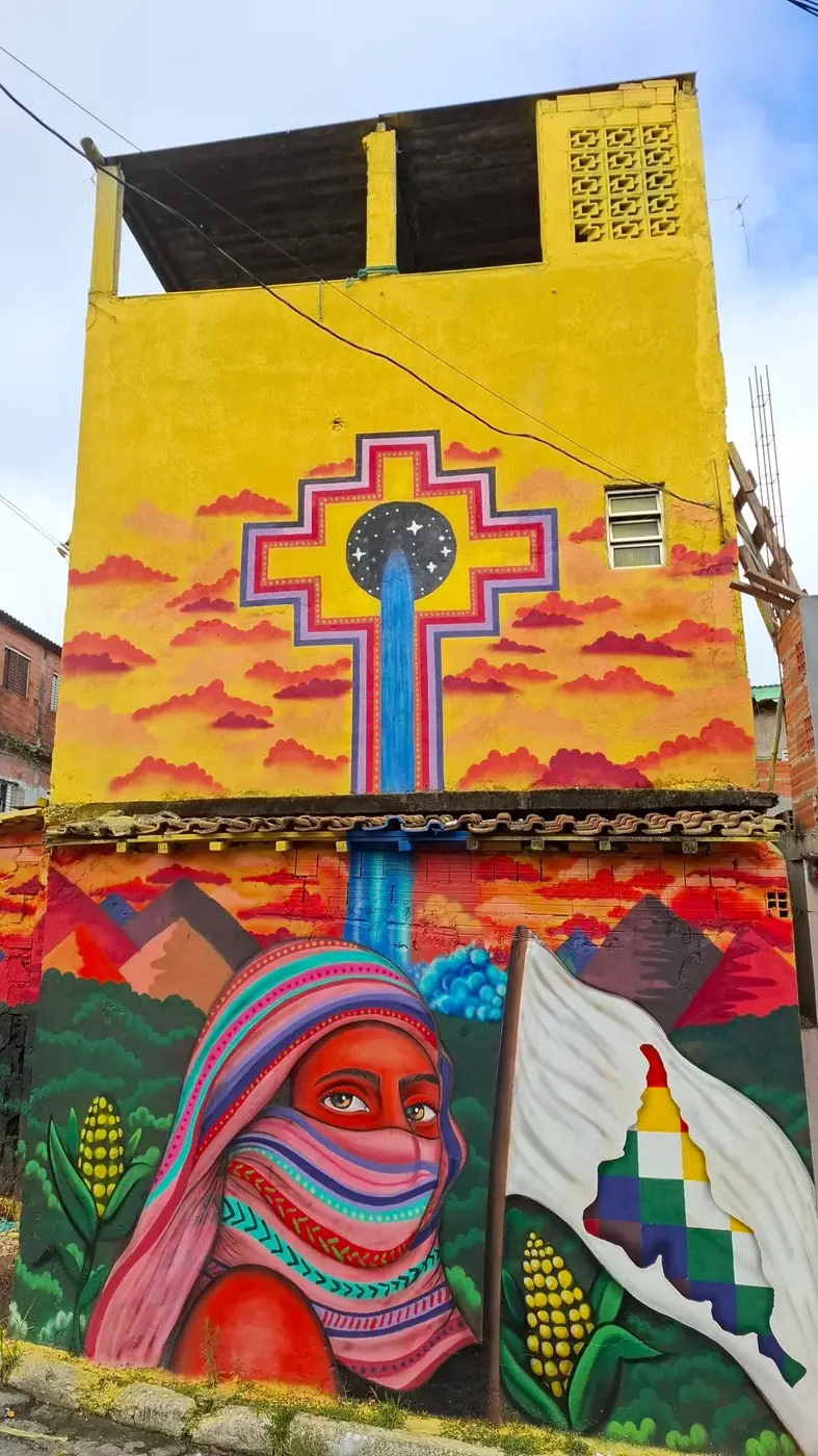 Mural da Favela Galeria em parede amarela, com figuras coloridas que remetem a paisagens e símbolos latino-americanos.