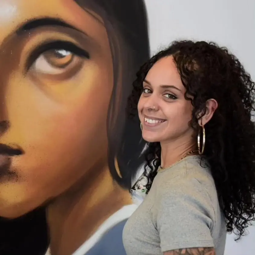 Quel sorri ao lado de uma pintura sua, um rosto feminino em tons de terra.